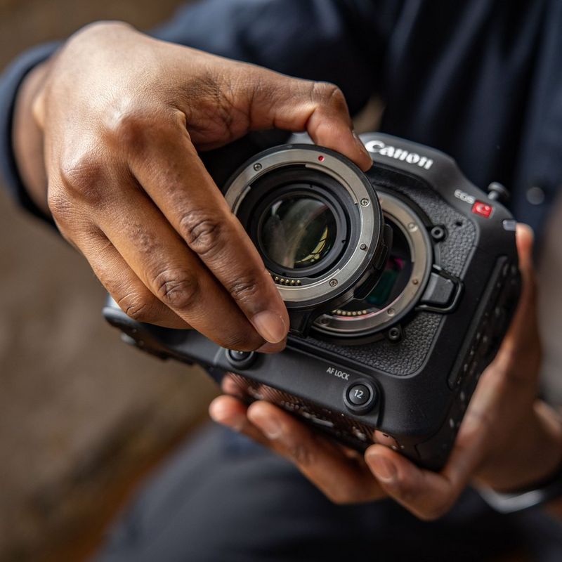 Een close-up van de handen van een gebruiker die de Canon-vattingadapter EF-EOS R 0.71x bevestigt op een Canon EOS C70-camera.