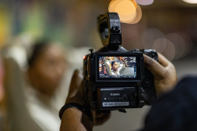 Het scherm op de achterkant van een Canon EOS C70, waarop een vrouw met haar armen omhoog achter haar hoofd zichtbaar is.