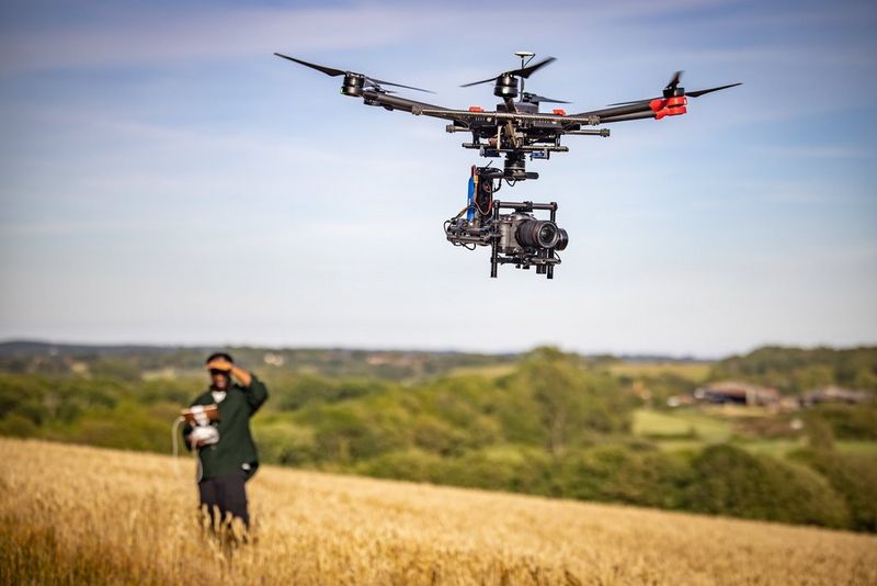 Een persoon bedient een drone waaraan een Canon EOS C70-camera is bevestigd en die op een zonnige dag over een korenveld vliegt. 