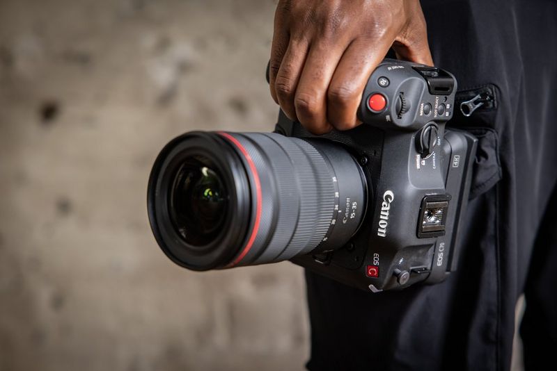 The Canon EOS C70 held in a man's hand by his side. 