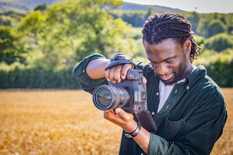 Le cinéaste Jolade Olusanya filmant avec la caméra Canon EOS C70 dans un champ, avec une végétation luxuriante en arrière-plan.