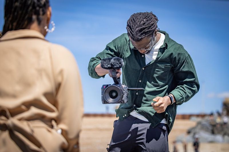 Holding the EOS C70 in one hand, a filmmaker stares intently at the display screen, his subject in the foreground.