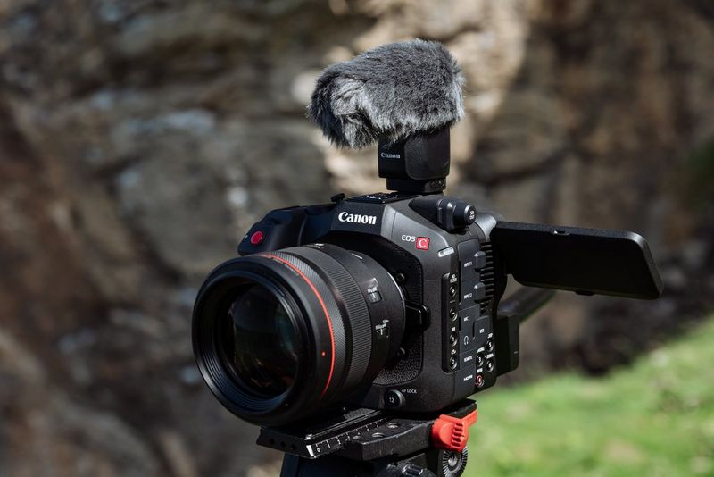 A Canon EOS C80 camera mounted on a tripod, featuring a large lens and an external microphone with a furry wind cover on top.