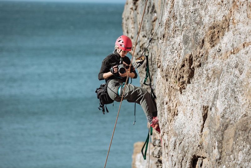Cinematographer Carolina Nunes suspended with safety ropes in midair on a cliff edge in Wales while filming with the Canon EOS C80 camera.