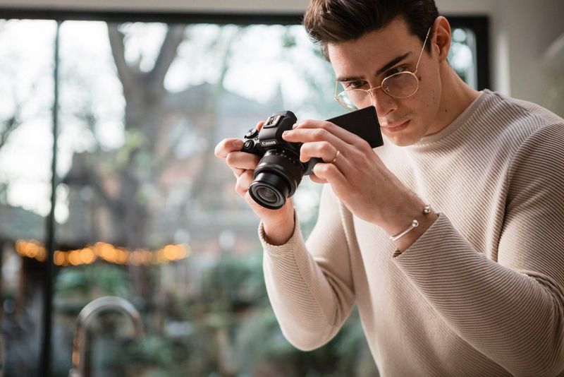 Мужчина в бежевом свитере и очках смотрит на экран с переменным углом наклона камеры Canon M50 Mark II.