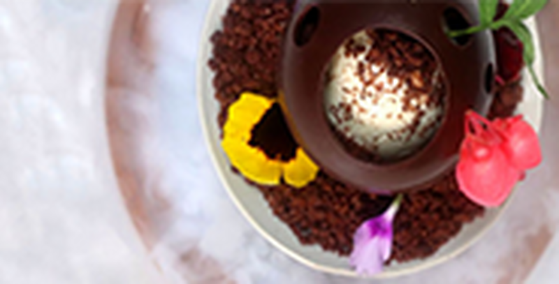 A hollow chocolate ball filled with ice cream and garnished with petals and chocolate sprinkles. 