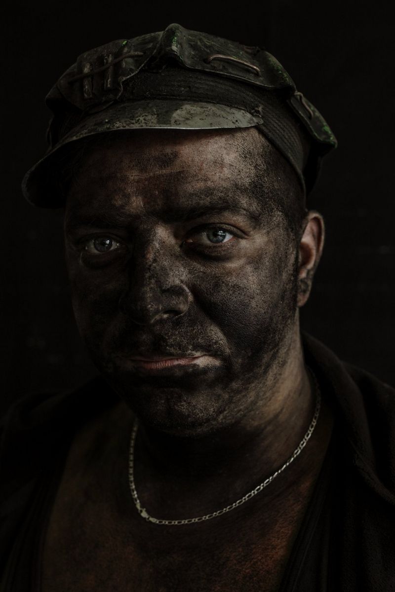 Een mijnwerker van wie het gezicht is bedekt met zwart stof, kijkt naar de camera in een foto die is gemaakt door Daniel Etter met een Canon EOS R.