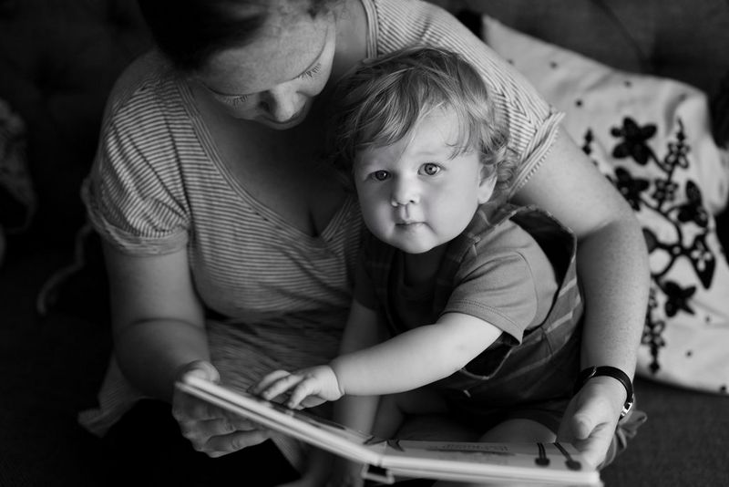 צילום שחור-לבן מלמעלה למטה של ​​אם וילד הקוראים ספר. הילד מרים את מבטו אל המצלמה תוך שהוא מושיט יד קדימה כדי להפוך את הדף.