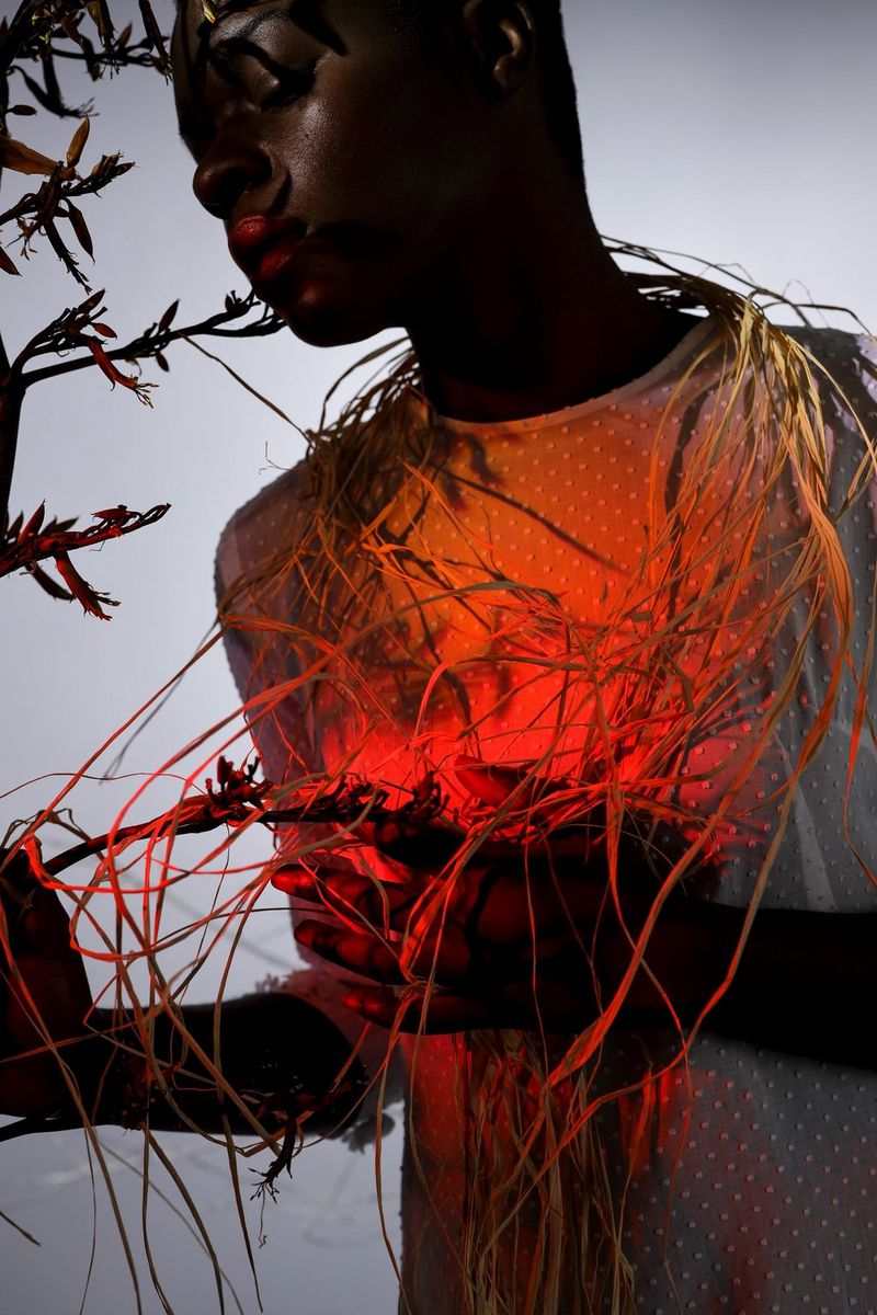 Een model wordt verlicht met een rood licht en is gewikkeld in lianen.