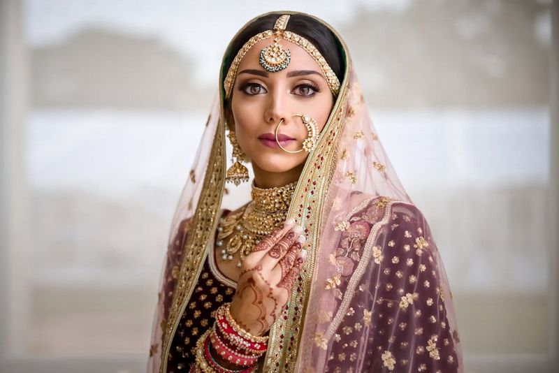 כלה לבושה בסארי מסורתי, מעוטרת בתכשיטי זהב וציורי חינה דקורטיביים מכסים את ידה.