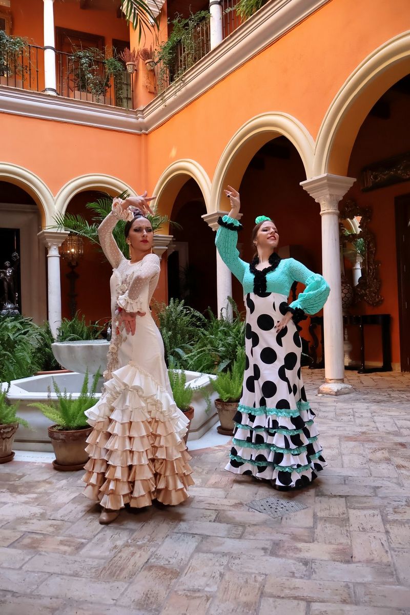 Deux danseuses de flamenco prennent la pose devant une fontaine dans une cour avec un sol carrelé et de riches colonnades orange en arrière-plan. Photo de voyage prise avec un objectif zoom Canon RF-S 18-45mm F4.5-6.3 IS STM.