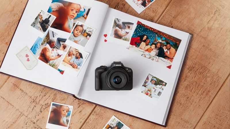 Камера Canon EOS R100 лежит на фотоальбоме на деревянном столе в окружении семейных фотографий.