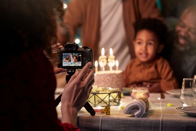 Человек настраивает камеру Canon EOS R100 на штативе-моноподе Canon для съемки ребенка с тортом ко дню рождения.