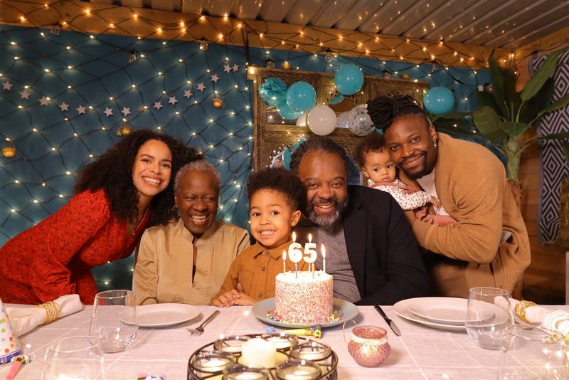 Семья улыбается, собравшись вокруг торта со свечами по случаю 65-летия; фото сделано на Canon EOS R100.