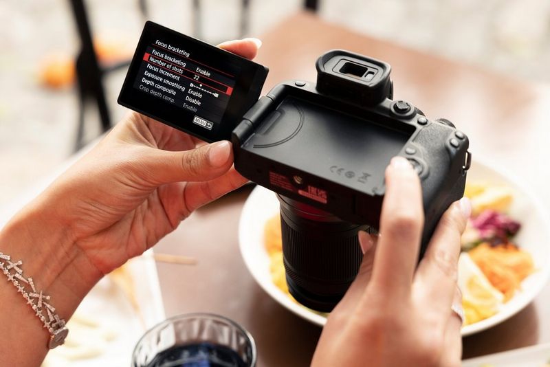 A pair of hands holds a Canon EOS R10, with the camera's screen showing focus bracketing settings.