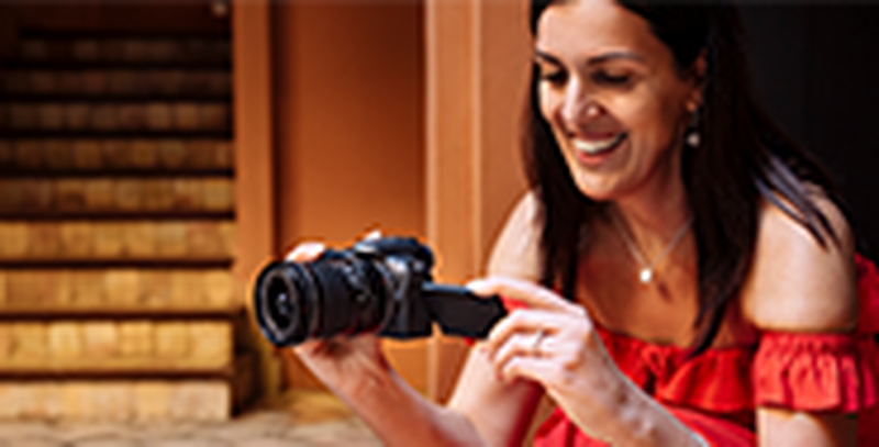 A woman wearing a red strapless dress crouches down to take a picture with a Canon EOS R10.