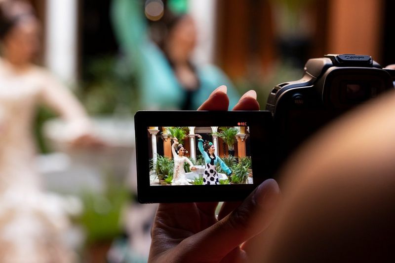 A view over the photographer's shoulder looking at the vari-angle touchscreen of a Canon EOS R10 showing two Flamenco dancers. The camera is set to record.