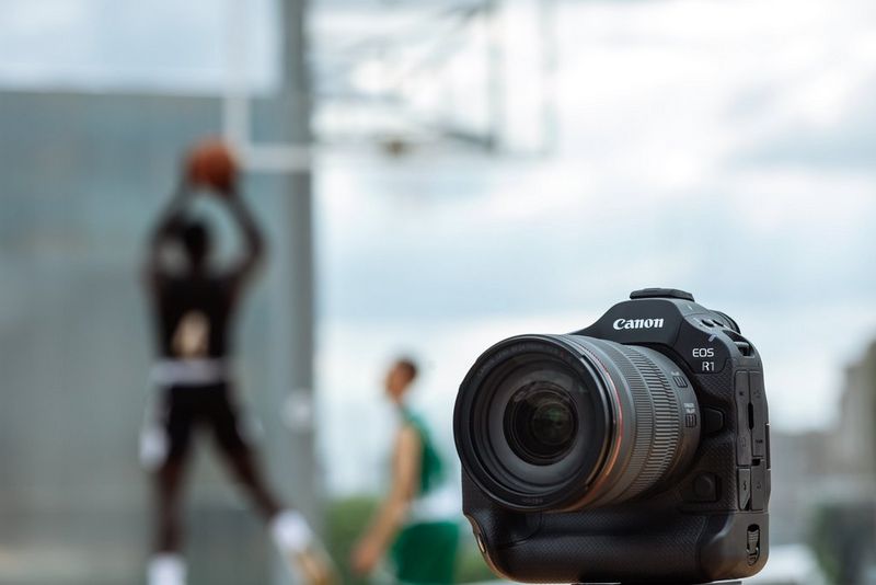 A Canon EOS R1 camera with a Canon RF 24-70mm F2.8L IS USM lens, pictured with basketballers out of focus in the background.