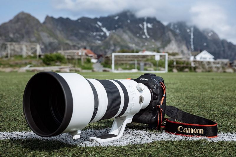 Een Canon EOS R1-camera ligt op de grond van een voetbalveld met rotsachtige bergen op de achtergrond.