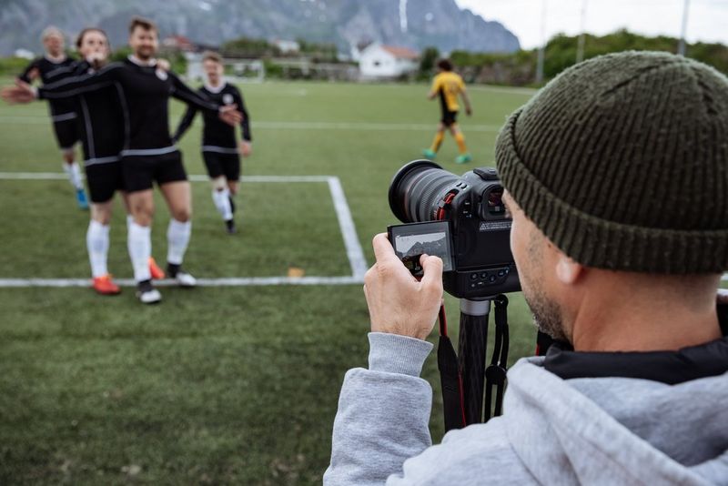 Een videograaf gebruikt een Canon EOS R1 om feestende voetballers op het veld te filmen.