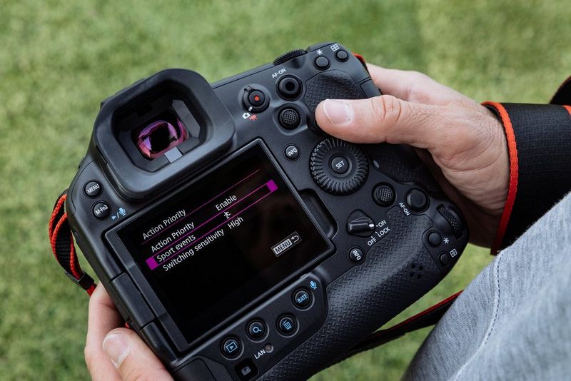 Фотограф держит в руке камеру Canon EOS R1 с открытым на ней экраном настроек приоритета действия.