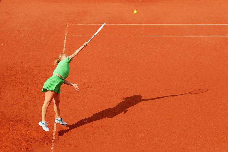 Un joueur de tennis photographié à grande vitesse sur un court en terre battue rouge, la balle figée en plein vol. Photo prise avec un Canon EOS R1 équipé d'un objectif Canon RF 24-70mm F2.8L IS USM.