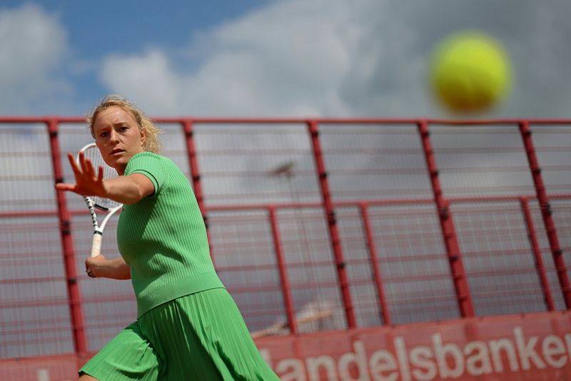 A photo taken on a Canon EOS R1 with a Canon RF 50mm F1.2L USM lens, capturing a tennis player in the act of drawing back to hit a ball travelling at speed towards her.
