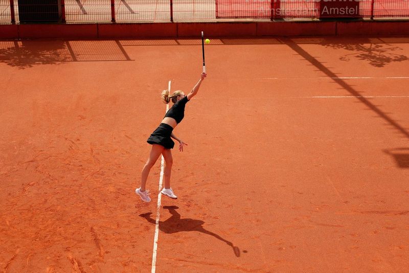 Een tennisser met zwarte kleding reikt met haar racket om de bal te raken, die in de lucht hangt. Gefotografeerd met een Canon EOS R1.