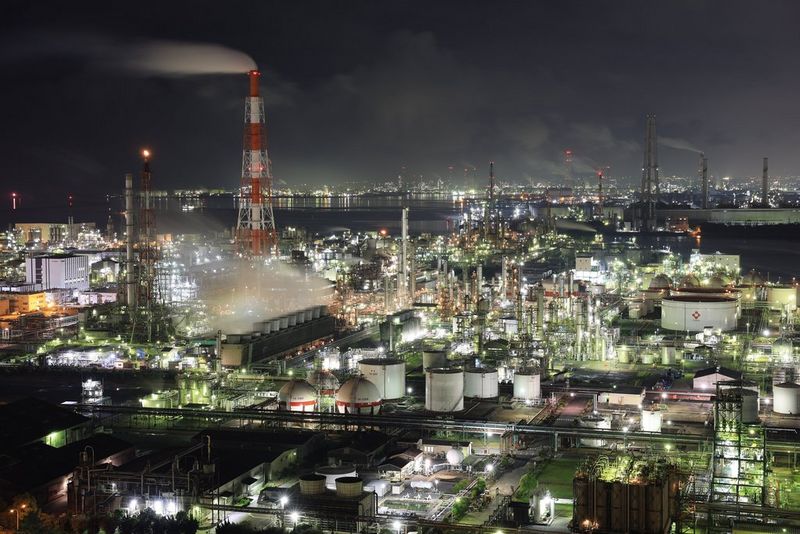 A large industrial plant and its surroundings at night. The plant is highly illuminated and in the background the outline of a city can be seen. Taken on a Canon EOS R3.