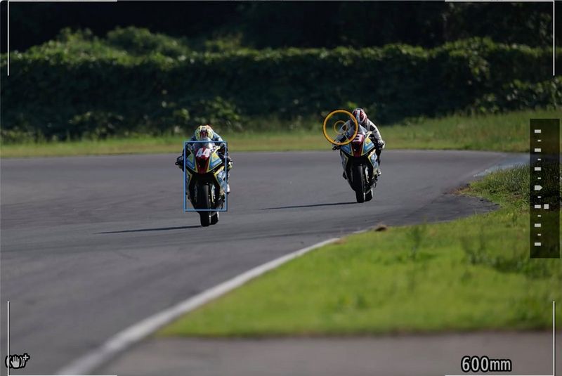 The view in a Canon EOS R3 viewfinder showing the active AF point as a blue box over a motorbike and the Eye Control AF point as an orange circle over another.