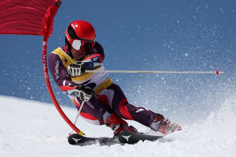 A skier slides around a flag on a course, snow spraying into the air from their skis.