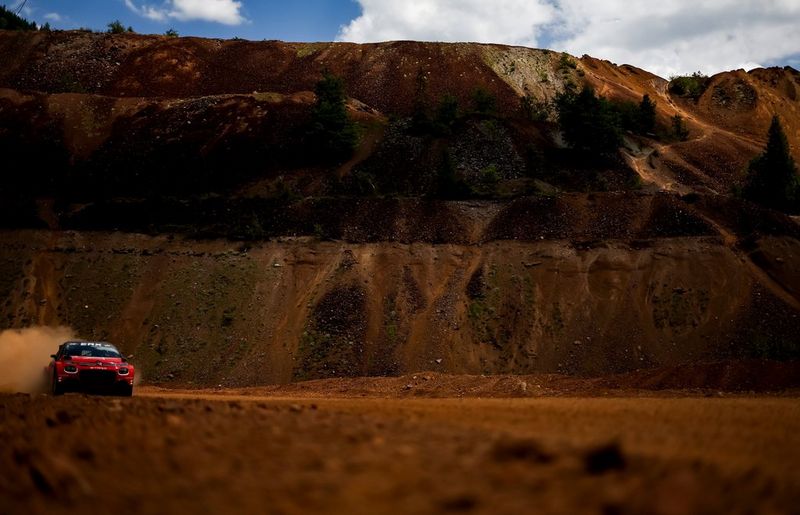 In a photo taken by Vladimir Rys with a Canon EOS R3, a Formula E rally car is captured entering the frame at the far left, in sharp focus against a rugged cliff face.