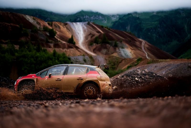 An electric rally car speeds through rocky terrain, throwing up mud and dust as it races along. 
