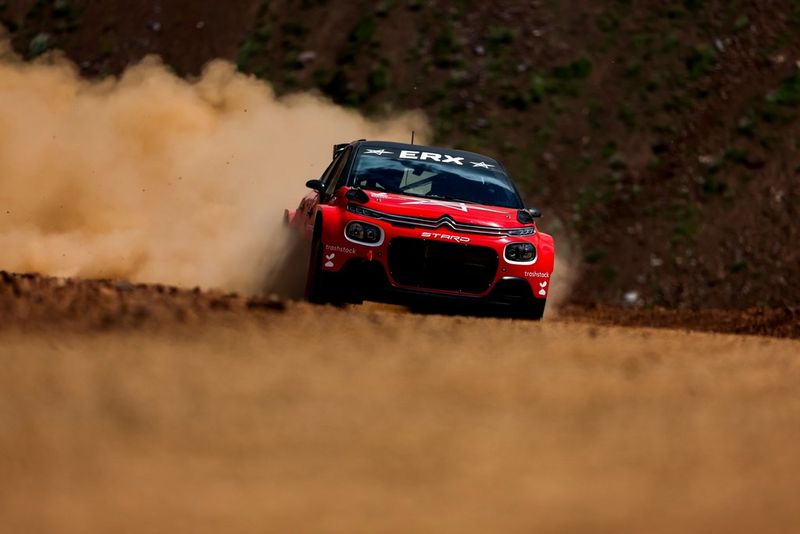 Un'auto da rally rossa, immortalata con una fotocamera Canon EOS R3, che solleva una nuvola di polvere sulla pista sterrata.