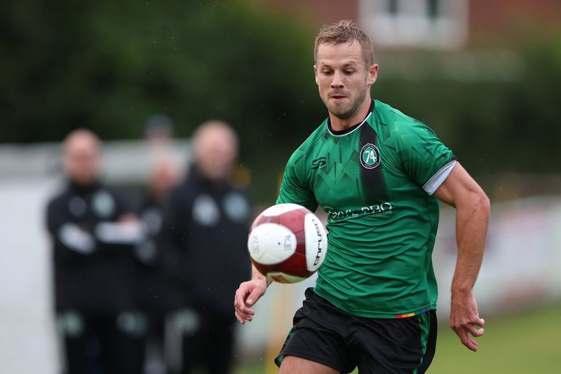 Een close-up van een voetballer in een groen shirt die de bal op zijn borst opvangt.