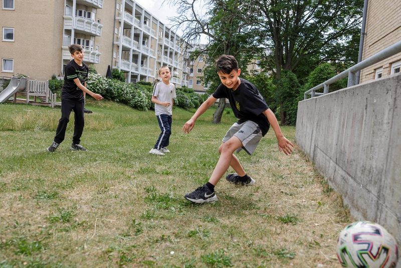 Drie jongens voetballen op een grasveldje bij een flatgebouw.