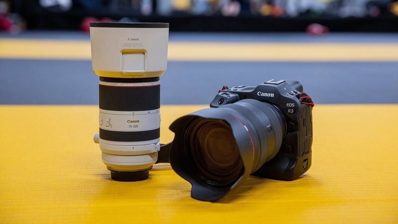 Een Canon EOS R3 en een Canon RF 70-200mm F2.8L IS USM-objectief liggen op de gele vloer van een boksring