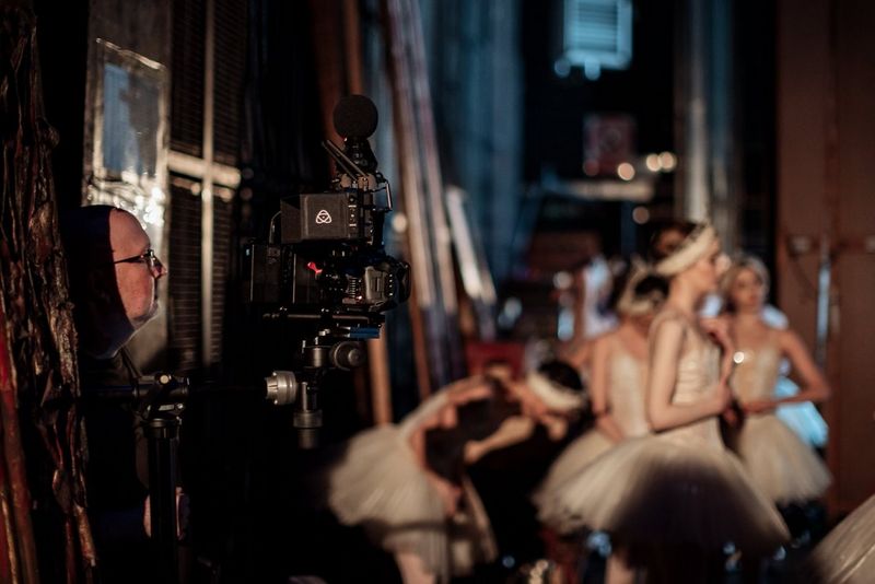 Mark Fensome staat met een Canon EOS R5 C en een Canon RF 5.2mm F2.8L DUAL FISHEYE-lens in de coulisse van een podium, met ballerina's op de achtergrond.