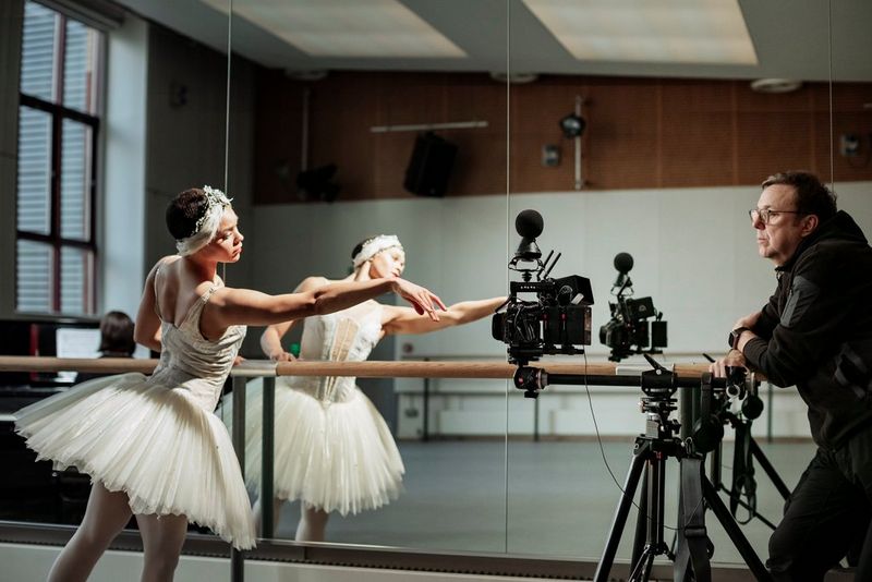 A ballerina stretches out in front of a ballet barre and wall mirror, being filmed by Clive Booth on a Canon EOS R5 C with a Canon RF 5.2mm F2.8L DUAL FISHEYE lens.