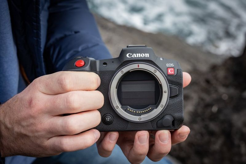 Mani che reggono una videocamera ibrida Canon EOS R5 C, su cui è visibile un obiettivo con innesto RF.