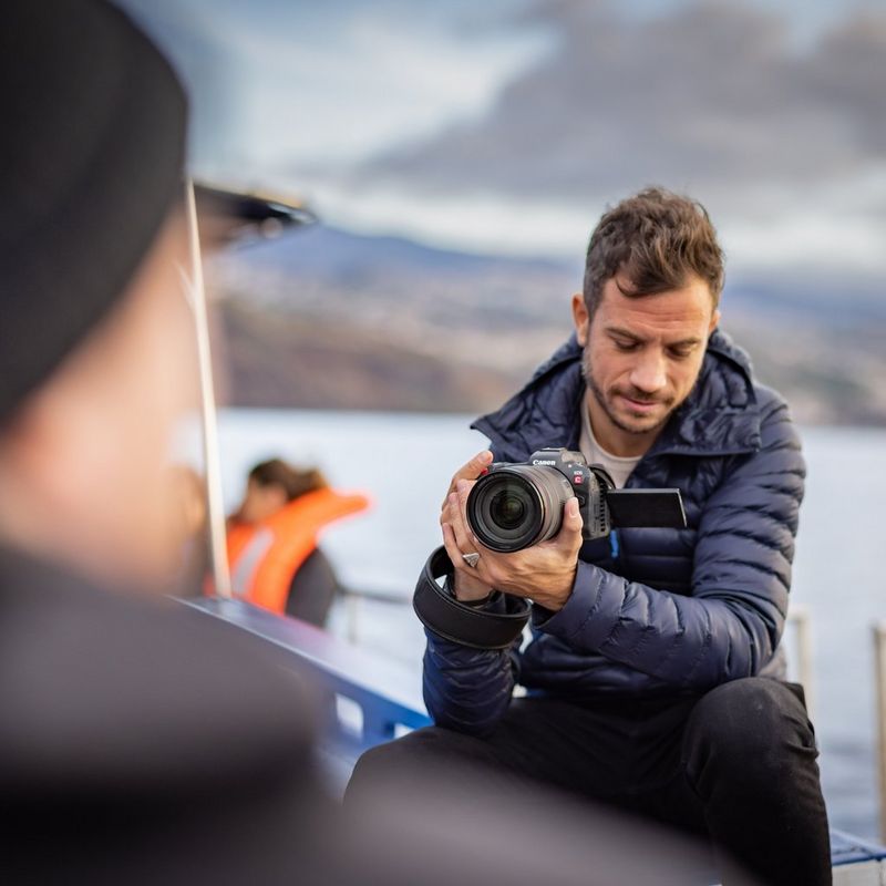 A man sat on the edge of a boat filming with a Canon EOS R5 C camera.