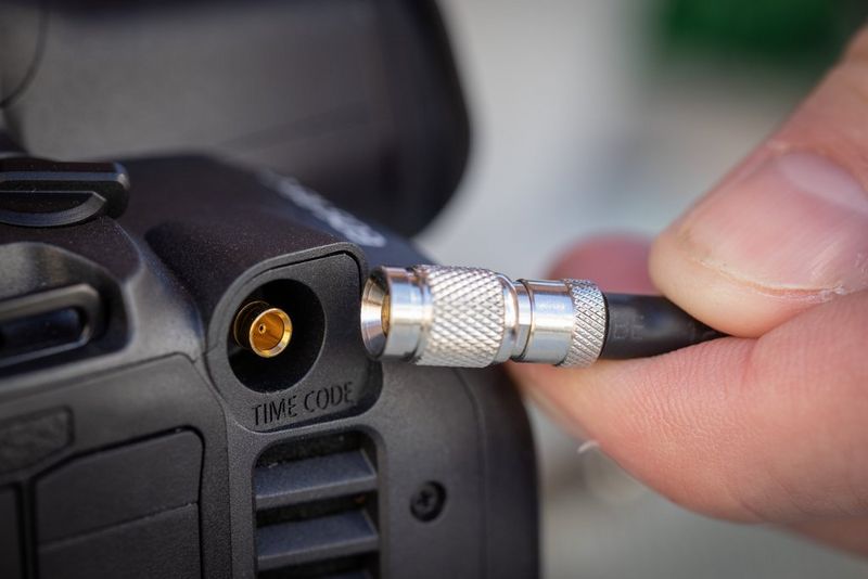 An index finger and thumb holding a cable next to the timecode in/out port on a Canon EOS R5 C. 