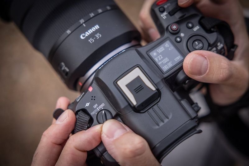 Hands holding an EOS R5 C camera, moving the three-way power switch to select video mode.