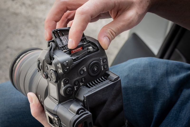 Mani che sorreggono una videocamera ibrida Canon EOS R5 C, con un dito che spinge una scheda di memoria in uno dei due slot dedicati.