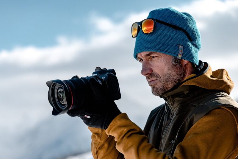 A photographer wearing a winter jacket, hat and gloves holding a Canon EOS R5.