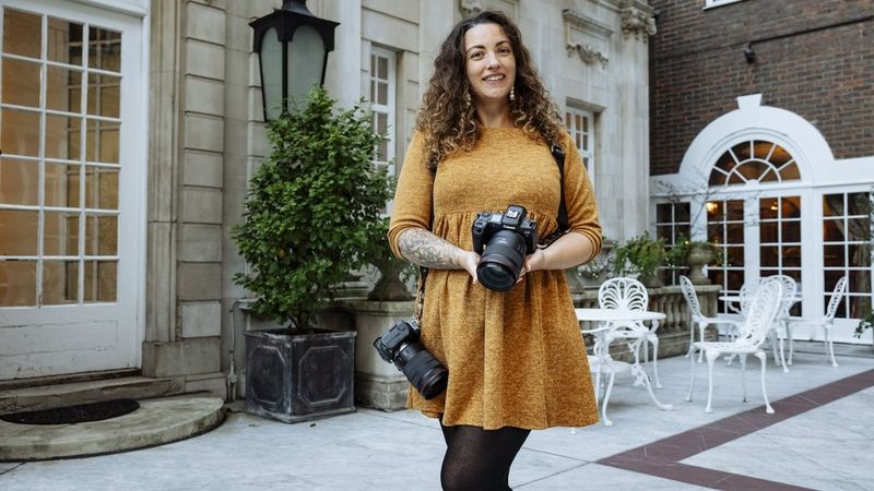 La fotografa Alison Bounce tiene in mano Canon EOS R5 e ha un'altra fotocamera appesa alla spalla.