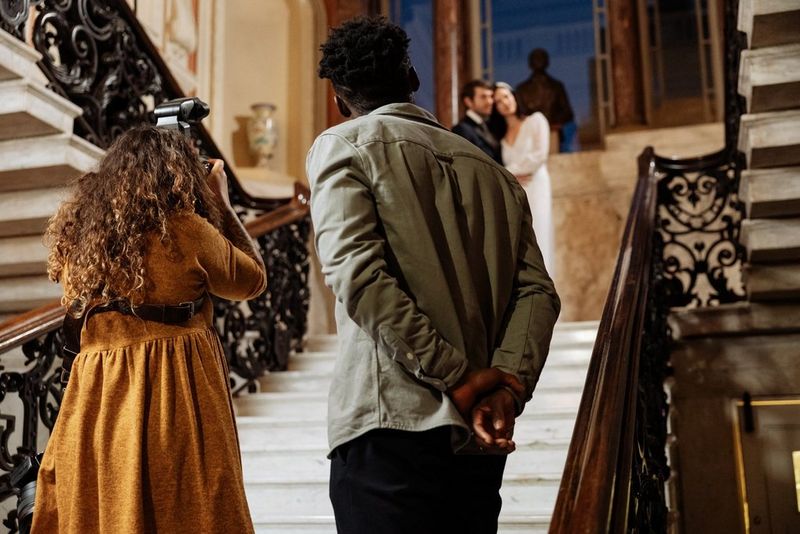 Alison Bounce stands at the bottom of a grand staircase and photographs a couple embracing at the top.