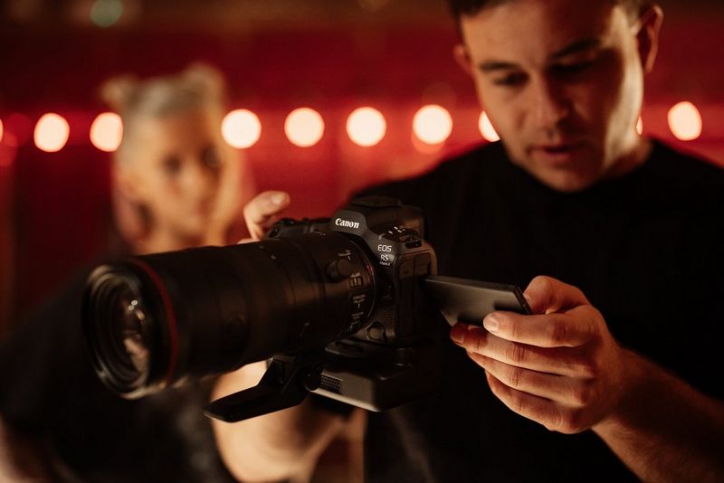 A man operates the touchscreen of a Canon EOS R5 Mark II with Cooling Fan CF-R20EP grip attached.