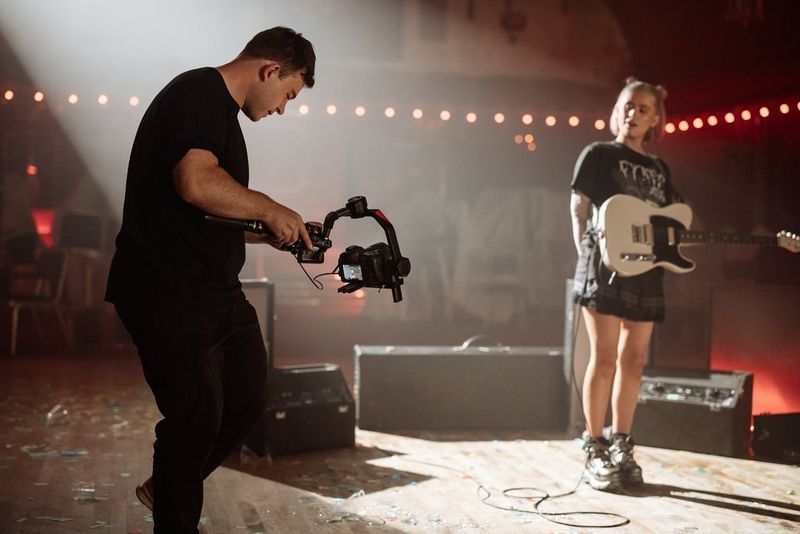 A filmmaker uses a Canon EOS R5 Mark II on a gimbal to film a guitarist on stage.