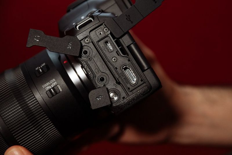 Een hand die de Canon EOS R5 Mark II-camera zo vasthoudt dat een aantal poorten en aansluitingen zichtbaar zijn.